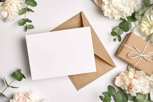 Invitation or greeting card mockup with envelope, gift box and white peony flowers and eucalyptus twigs - Foto, imagen