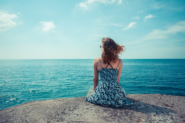 Молода жінка сидить біля океану
 - Фото, зображення