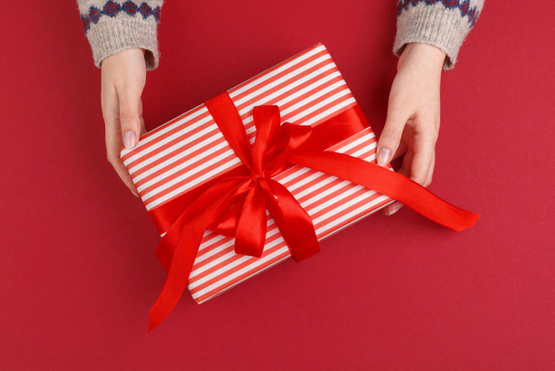 Female hands with christmas gift on red background, top view, copy space - Foto, immagini