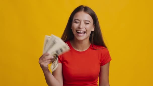 Fröhliche Frau, die Geld in der Hand hält und Dollar-Banknoten wirft, gelber Hintergrund - Filmmaterial, Video