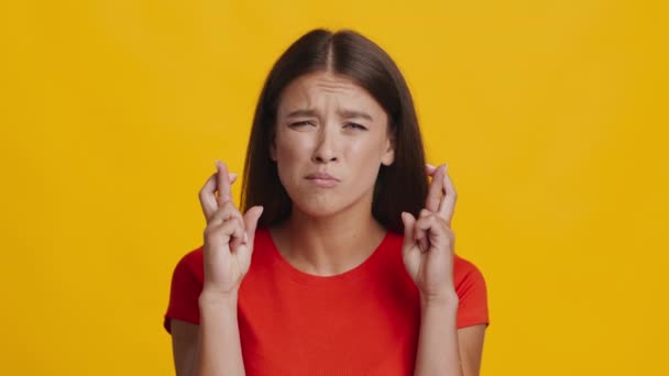Millennial kobieta trzyma kciuki za szczęście na żółtym tle - Materiał filmowy, wideo