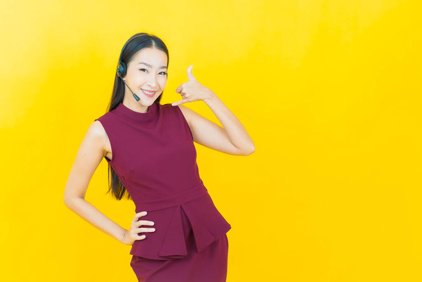 Retrato bela jovem mulher asiática com call center centro de atendimento ao cliente no fundo de cor amarela - Foto, Imagem