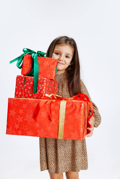 Portrat of beautiful little girl weraing holiday dress standing with huge gift, present box isolated on white studio background - Photo, image