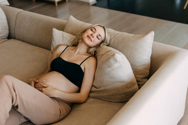 Těhotná žena nosí útulné domácí oblečení, leží doma na pohovce, sní. - Fotografie, Obrázek