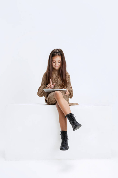 One little cute beautiful girl, kid in casual dress sitting on big box with digital tablet isolated on white studio background. - Φωτογραφία, εικόνα