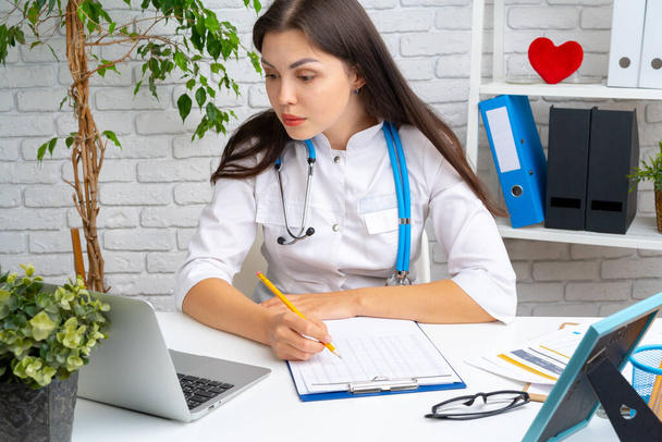 Jeune femme médecin cardiologue assise à son bureau et travaillant - Photo, image
