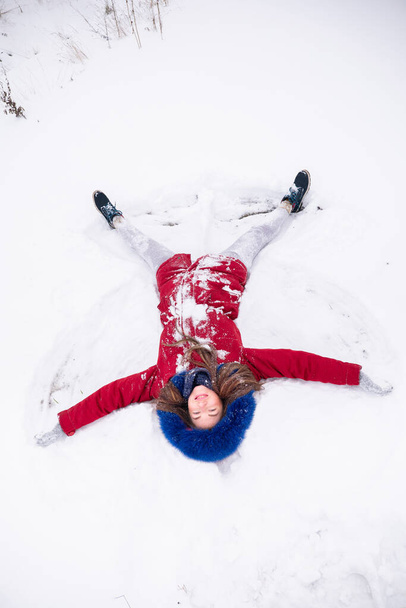 Young funny woman in red coat lying on the snow - Фото, изображение