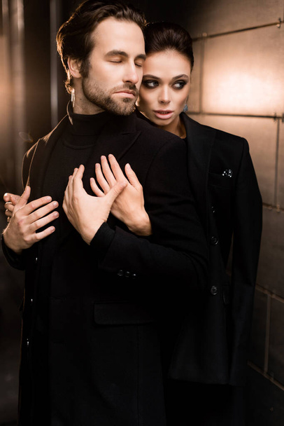 portrait of a beautiful young couple in a black suit and a jacket on a background of a dark room - Photo, Image