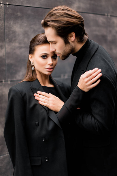 beautiful young couple in black suit and jacket posing on background of old building - Photo, Image