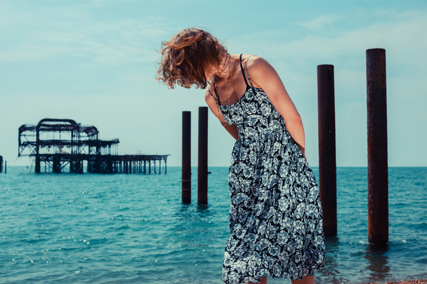 Young woman standing by the ocean with old pier - Fotoğraf, Görsel