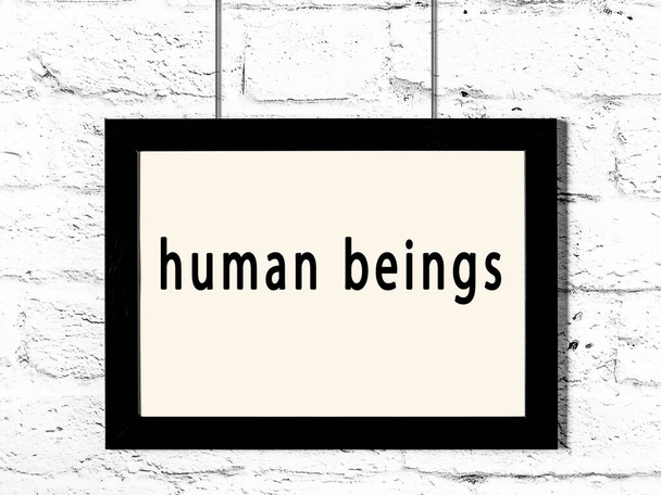 Černý dřevěný rám s nápisem lidské bytosti visící na bílé cihlové zdi  - Fotografie, Obrázek