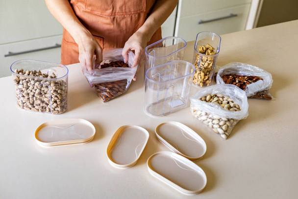 Primer plano ama de casa manos colocación de tuercas paquete de plástico en la caja del envase en la mesa de madera en la cocina - Foto, Imagen