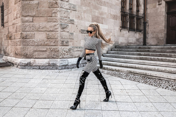Υψηλή μόδα. Σέξι γυναίκα σε κομψό ντύσιμο και μοντέρνα μπότες ποζάρει στην πόλη. Μοντέλα μόδας σε κομψό ντύσιμο. Κομψότητα. Φθινόπωρο, χειμερινή μόδα. - Φωτογραφία, εικόνα