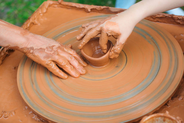 Teacher and kid making ceramic pot. Potters and child hands. Pottery workshop outside. Master teaching kid to creating on the pottery wheel. Grandmom teaches granddaughter pottery. Clay modeling. - Photo, Image