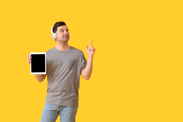 Молодой человек с планшетным компьютером и наушниками указывает на что-то на цветном фоне - Фото, изображение