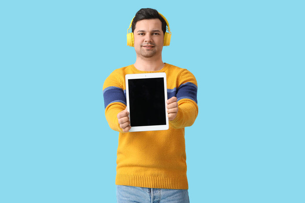 Hombre joven con tablet y auriculares sobre fondo de color - Foto, Imagen
