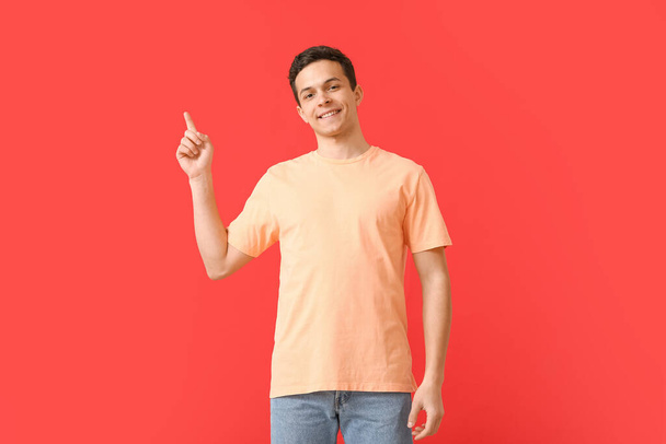 Handsome young man in stylish t-shirt pointing at something on color background - Photo, image