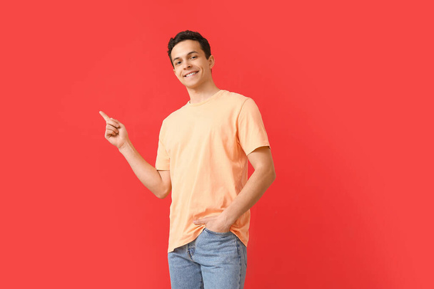 Schöner junger Mann in stylischem T-Shirt zeigt auf etwas auf farbigem Hintergrund - Foto, Bild