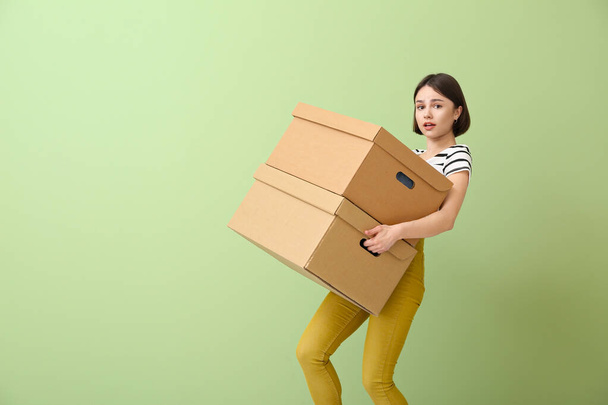 Bezorgde jonge vrouw met garderobe dozen op kleur achtergrond - Foto, afbeelding