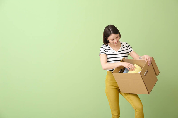 Młoda kobieta trzyma szafa pudełko z ubraniami na tle koloru - Zdjęcie, obraz