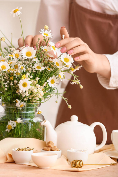 Woman with chamomile flowers and teapot on table - Фото, зображення