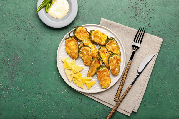 Plate with tasty jalapeno poppers, cheese and sauce on green background - Photo, Image