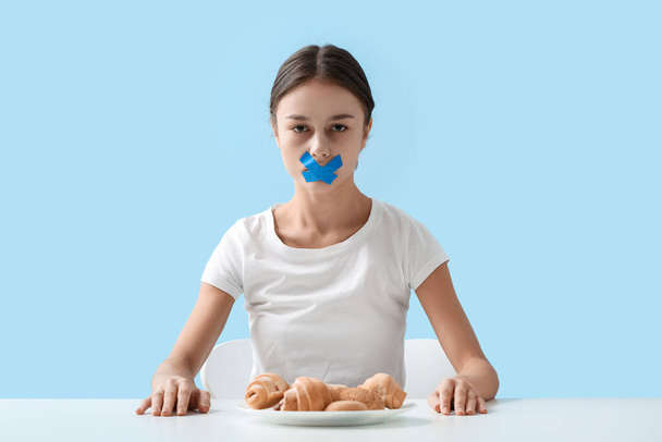 Junge Frau mit abgeklebtem Mund am Tisch vor farbigem Hintergrund. Magersucht-Konzept - Foto, Bild