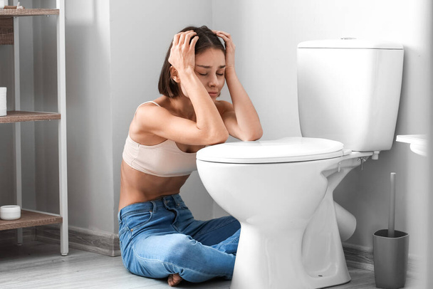 Young woman near toilet bowl in bathroom. Anorexia concept - Photo, Image