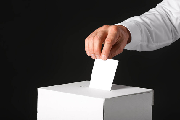 Szavazó férfi közelében szavazólap doboz sötét háttér - Fotó, kép