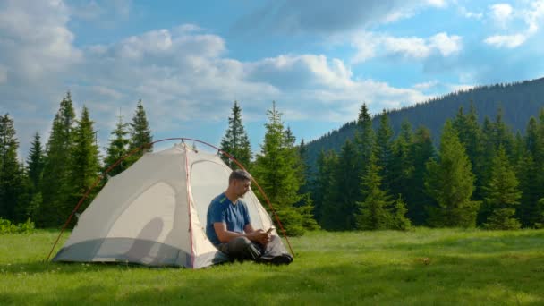 Un turista descansa en una tienda de campaña en un claro bosque en las montañas - Imágenes, Vídeo