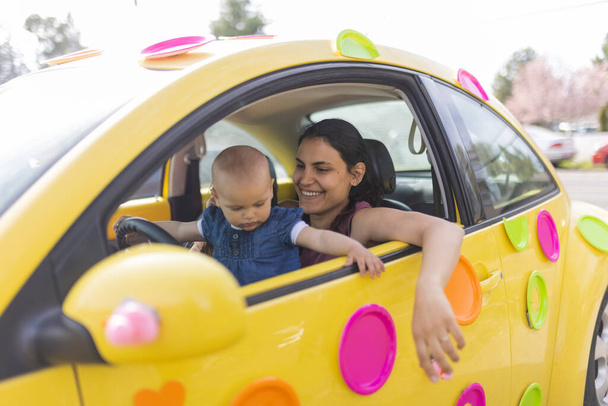 Gelukkig moeder en haar schattige baby in kleurrijke compacte auto - Foto, afbeelding