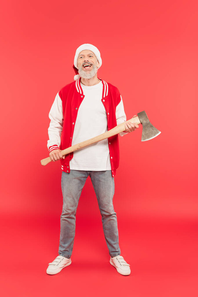 piena lunghezza di sorridente uomo di mezza età in cappello di Babbo Natale con ascia sul rosso - Foto, immagini