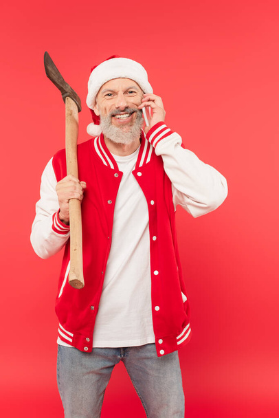 felice uomo di mezza età in cappello da Babbo Natale con ascia mentre parla su smartphone in rosso - Foto, immagini