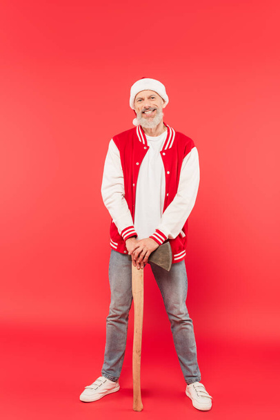 piena lunghezza di felice uomo di mezza età in cappello Santa ascia mentre in piedi sul rosso - Foto, immagini