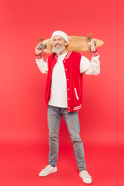 teljes hossza vidám középkorú férfi télapó kalap gazdaság gördeszka piros - Fotó, kép