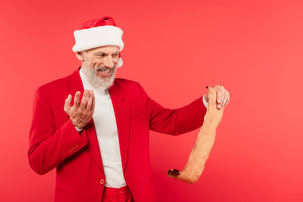 positiver reifer Mann mit Weihnachtsmann liest Brief auf Bastelpapier isoliert auf rotem Papier - Foto, Bild