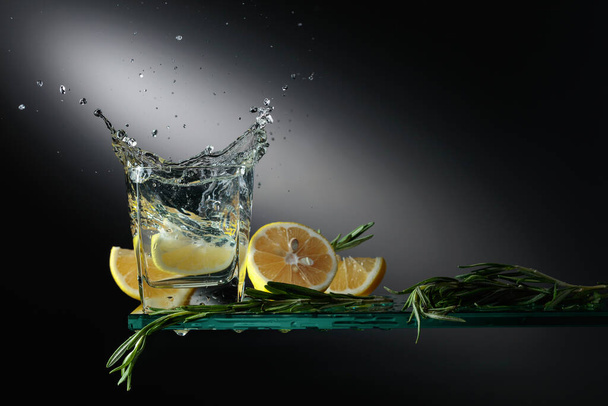 Gin a tonic koktejl s citronovými plátky a rozmarýnovými výhonky. Kousek citronu spadne do skla a vytvoří krásnou šplouchnutí. - Fotografie, Obrázek