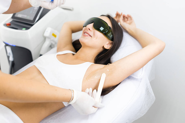 Cosmetoloog brengt gel voor laser ontharing aan vrouw oksel - Foto, afbeelding