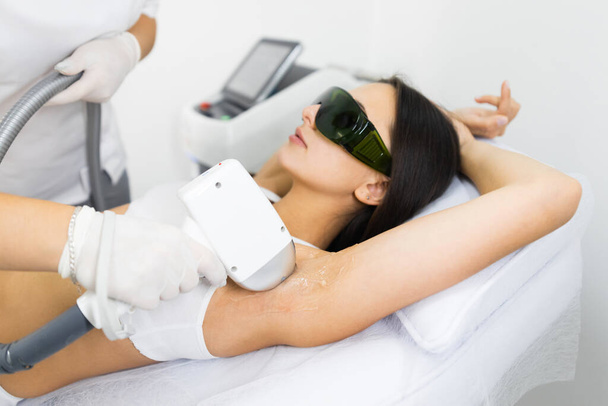 Woman in white underwear doing laser hair removal on armpits in epilation salon - Photo, Image