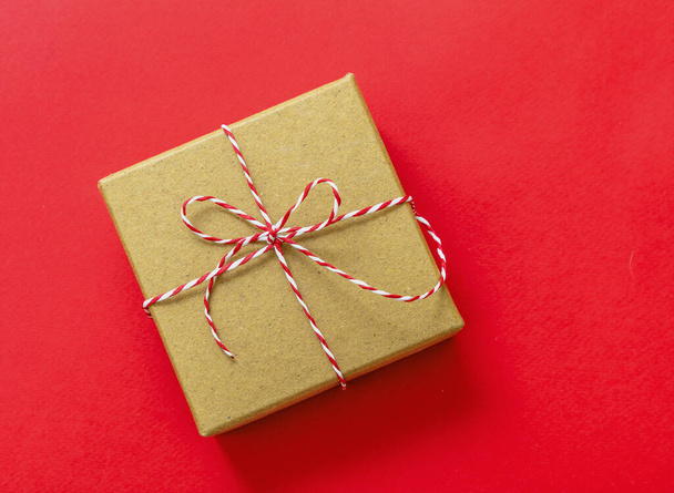 Weihnachtsgeschenkbox auf rotem Hintergrund, Draufsicht. Rot weiß gestreifte String gebundene Schleife auf braunem Kraftpapier vorhanden. Hausgemachte diy Öko-Feiertagsverpackung - Foto, Bild