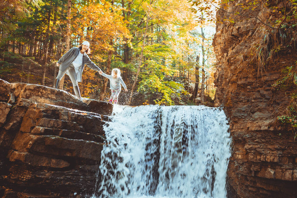 молода жінка з маленькою дівчинкою дивиться на водоспад осіннього лісу концепція пішохідного туризму
 - Фото, зображення