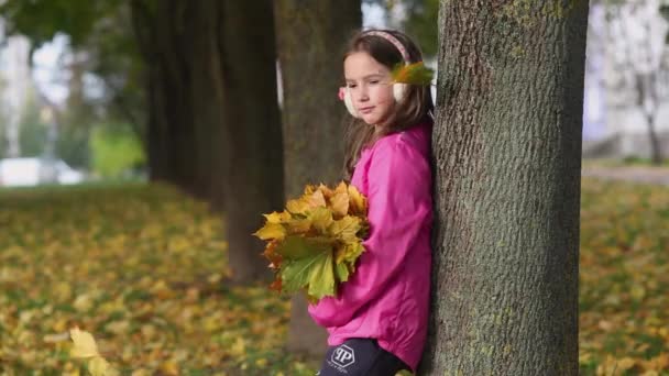 少女は手に葉の花束を持った公園の木の下に立っている。木から色の葉が落ちている。. - 映像、動画