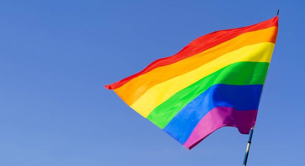 Gay rainbow flag waving in the wind in a clear blue sky - Фото, зображення
