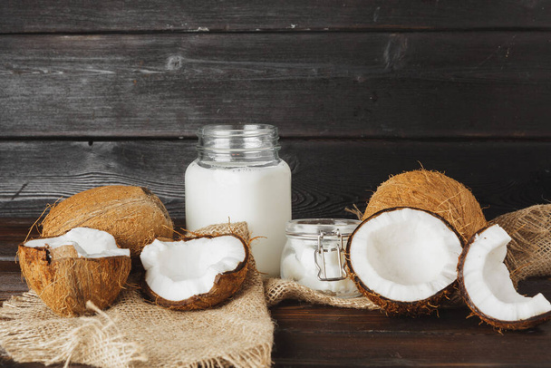 Broken coconut and coconut milk on black wooden background - Foto, Imagen