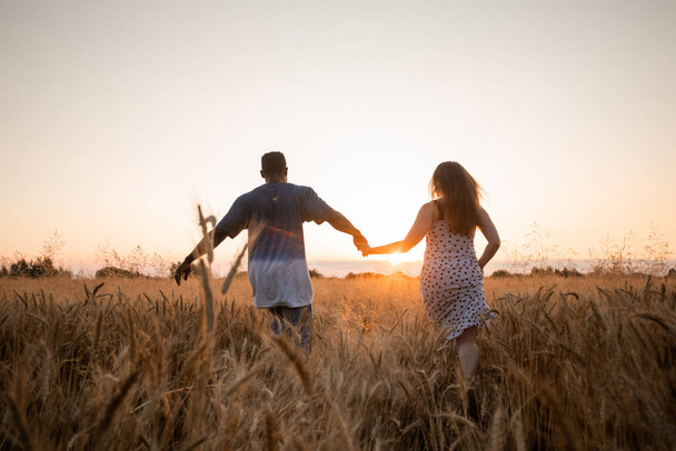 Young adult couple holding hands while walking in field - Fotografie, Obrázek