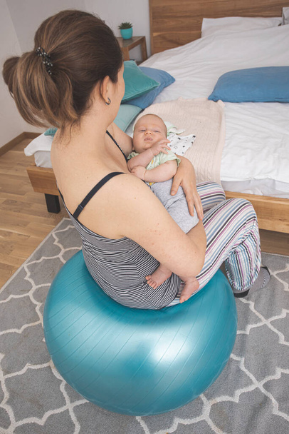 Mother holding and rocking baby sitting on fitball - Фото, изображение