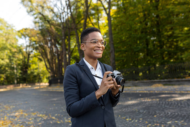 Surprised and happy African American woman looks at the camera and smiles holding a film camera on a walk in the park - Photo, image