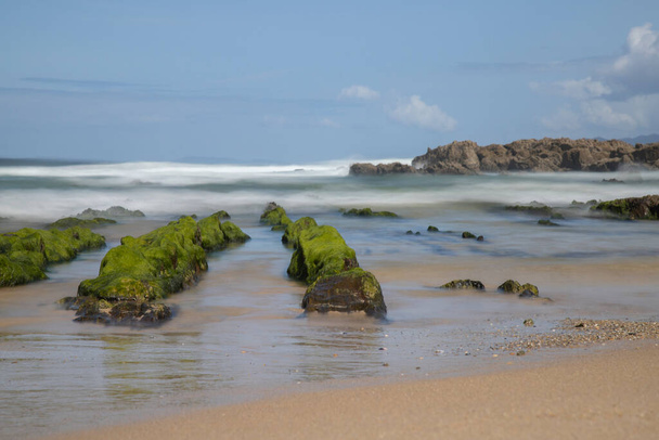 As Furnas beach long exposure picture showing extended rocks covered by green seaweeds under a blue sky in Galicia - Photo, Image