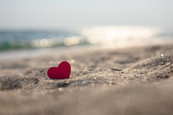 Маленьке червоне серце на піску на тлі боке з відблисків моря. Вибірковий фокус на серці, вузький фокус
. - Фото, зображення