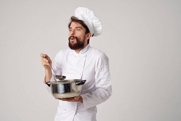 Aşçı kıyafetleri içinde elinde tencere tutan bir adam mutfakta yemek pişiriyor. - Fotoğraf, Görsel